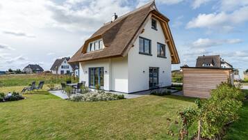 A modern house with a sloped roof, a patio with chairs, and a well-maintained lawn.