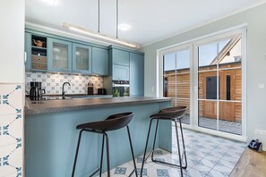 A modern kitchen with blue cabinets, a granite countertop, and two bar stools. - Holiday Home 'Maison Mer Baltique' with Sea View, Private Terrace and Wi-Fi (Dranske)