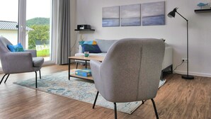 A modern living room with a sofa, armchair, coffee table, and artwork on the wall. - Holiday Home 'Christa' with Lake View, Private Terrace and Wi-Fi (Diemelsee)