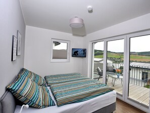 A bedroom with a bed, pillows, a TV, a window, and a balcony with a table and chairs.