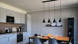 A modern kitchen with white cabinets, a microwave, and a coffee maker. There is a dining table with chairs and a hanging light fixture above. - Holiday Home 'Christa' with Lake View, Private Terrace and Wi-Fi (Diemelsee)