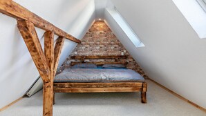 A loft bedroom with a sloped ceiling, exposed brick wall, and a wooden bed frame.