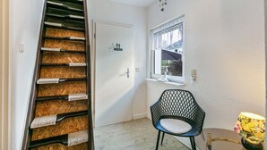 A staircase with a wooden finish, a white door with a lounge sign, a black chair, a window with a view, and a lamp on a table.