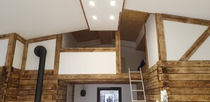 L’intérieur de la cabane est agrémenté de poutres apparentes, et comprend un espace en mezzanine ainsi qu’une échelle menant à l’étage supérieur.