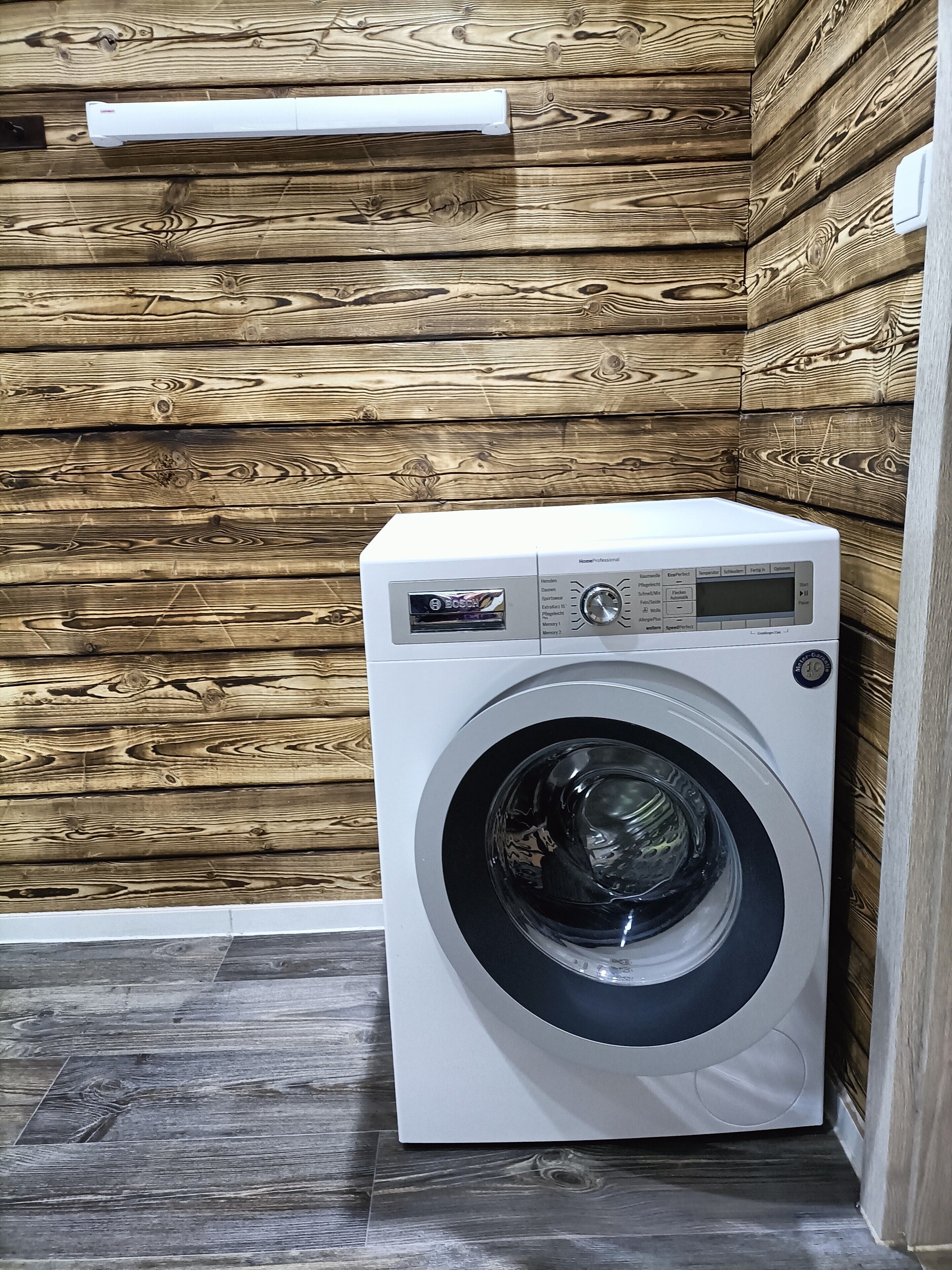 Un lave-linge à chargement frontal se trouve dans une pièce dont les murs sont recouverts de panneaux en bois et dont le sol est en bois foncé.