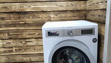 Un lave-linge à chargement frontal se trouve dans une pièce dont les murs sont recouverts de panneaux en bois et dont le sol est en bois foncé.
