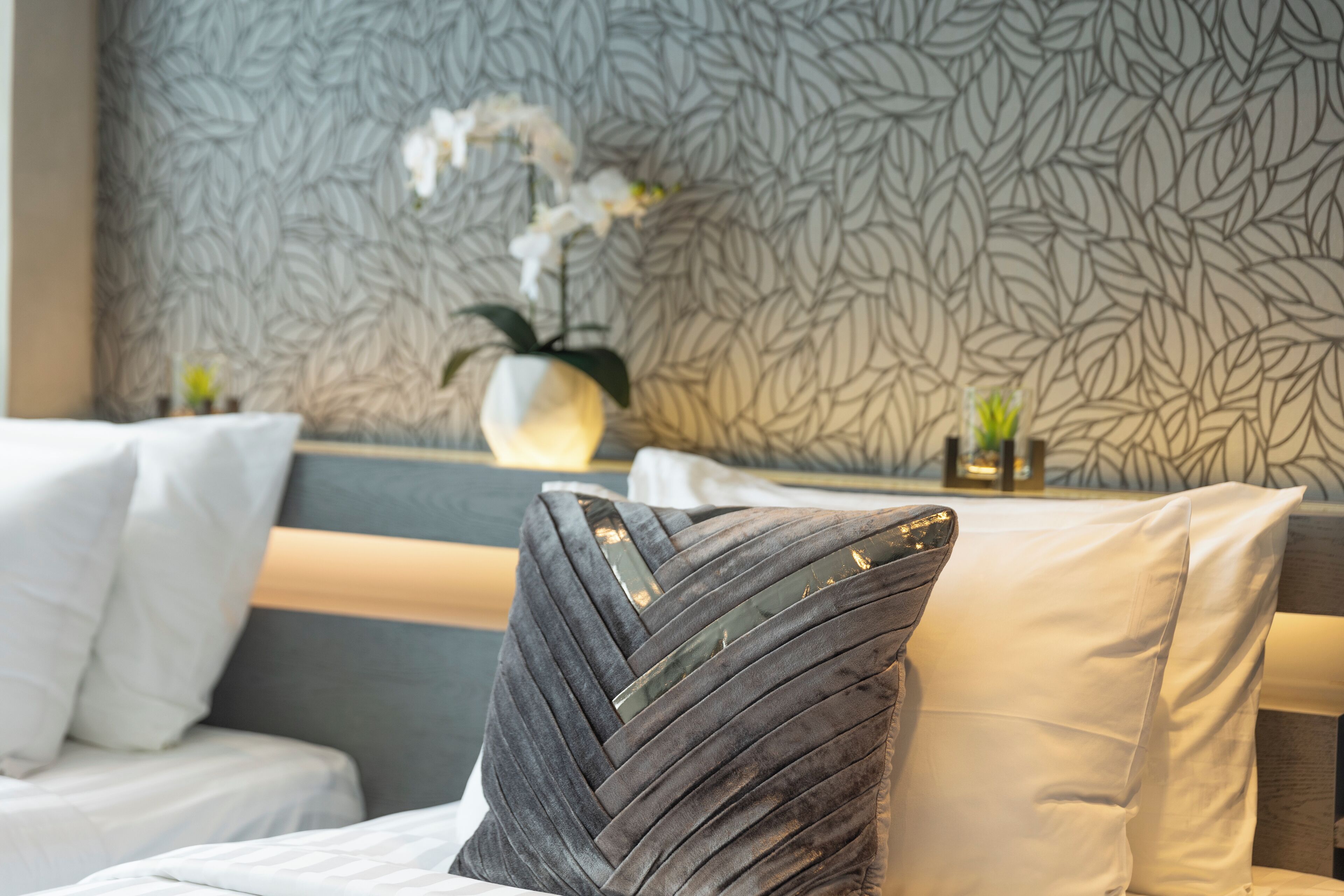 A hotel room with a patterned wallpaper, a bed with white bedding, and a decorative pillow.