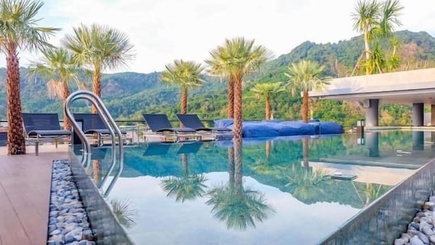 Piscina límpida com espreguiçadeiras e palmeiras, emoldurada por uma paisagem montanhosa.