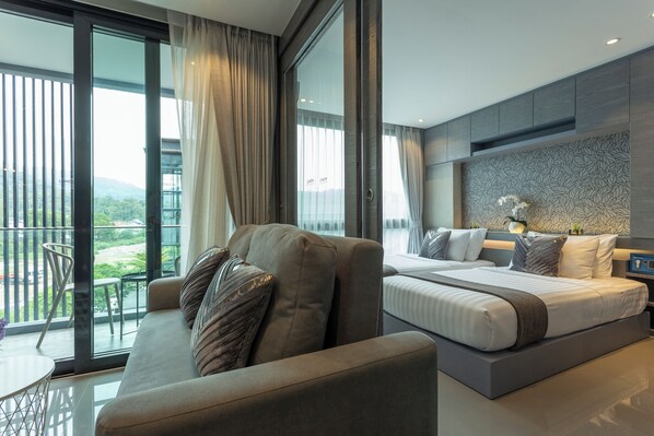 A modern bedroom with a large bed, a sofa, and a balcony with a view of greenery.