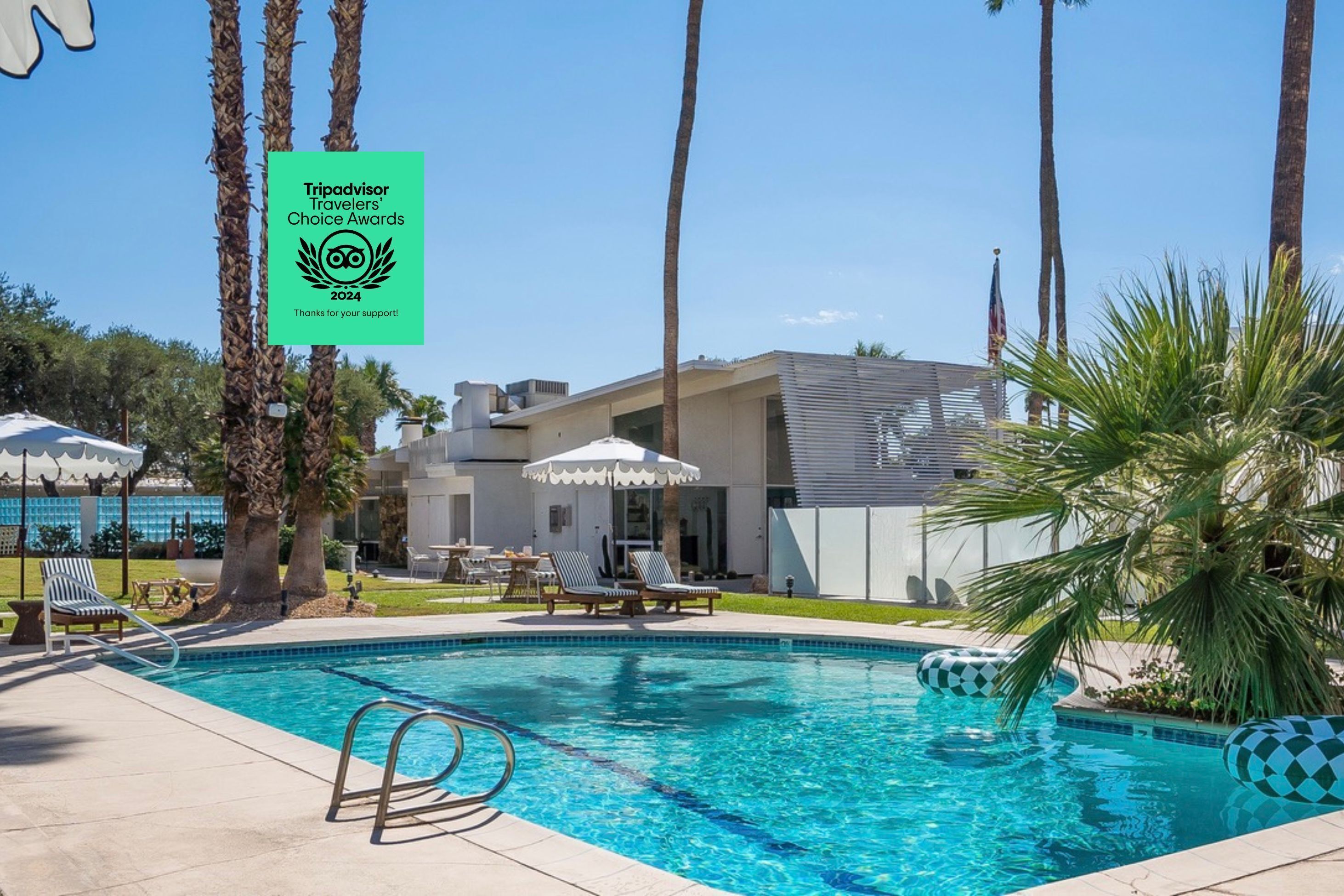 A swimming pool with lounge chairs and umbrellas, surrounded by palm trees and a modern building.