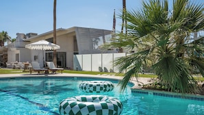 Une piscine avec deux bouées gonflables à motifs à carreaux, des chaises longues et un palmier.