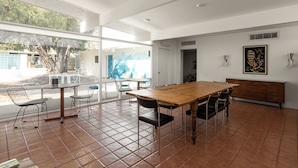 Un vaste espace dédié à la salle à manger, avec une table et des chaises en bois, de grandes fenêtres et une vue sur l’extérieur.