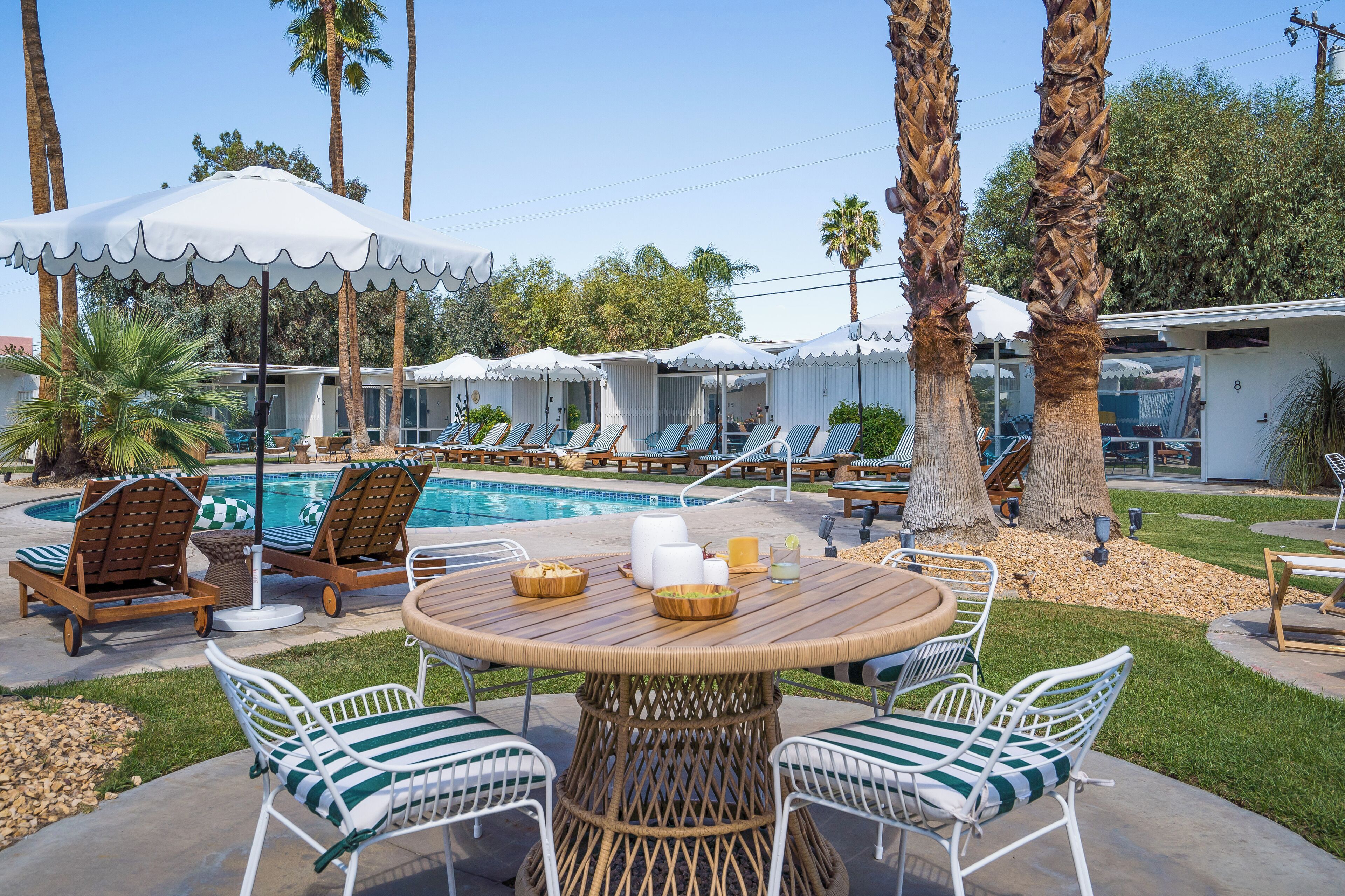 Zona de piscina con sillones reclinables, sombrillas y una mesa de comedor.
