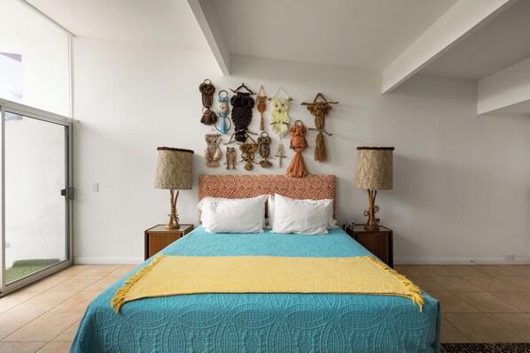 Un dormitorio con una cama, dos mesitas de noche, una lámpara y una pared decorada con objetos.
