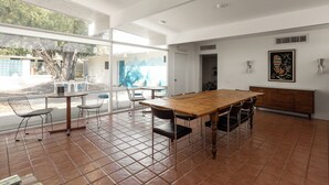 A spacious dining area with a wooden table and chairs, large windows, and a view of the outdoors. - Patio, Pool, Firepit | Queen Studio at Monkey Tree (Palm Springs)