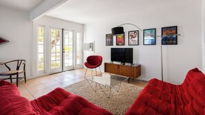 Ein Wohnzimmer mit einem roten Sofa, einem Glastisch, einem roten Sessel, einem Fernseher auf einem Holzschrank und einer Glastür.