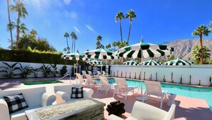 A poolside area with lounge chairs, umbrellas, and a stone fire feature.