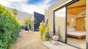 A modern building with a large glass door leading to a bedroom with a bed and a nightstand.