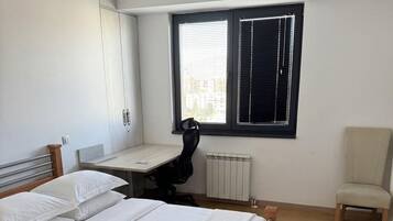 Ein Schlafzimmer mit einem hölzernen Bett, einem Schreibtisch, einem Stuhl und einem Fenster mit Jalousien.