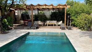 A rectangular swimming pool with tiled edges, surrounded by a patio area with lounge chairs and a pergola with a thatched roof. - Outbuilding of a 4-star house, swimming pool, patio, private parking, air conditioning, sleeps 2/3 (La Ciotat)