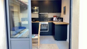 A modern kitchen with dark cabinetry, a built-in oven, a microwave, and a coffee machine. - Outbuilding of a 4-star house, swimming pool, patio, private parking, air conditioning, sleeps 2/3 (La Ciotat)