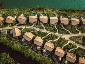 Eine Luftaufnahme eines Resorts mit mehreren Bungalowunterkünften, von denen jede einen privaten Pool besitzt, umgeben von üppiger Vegetation und einem gewundenen Weg.