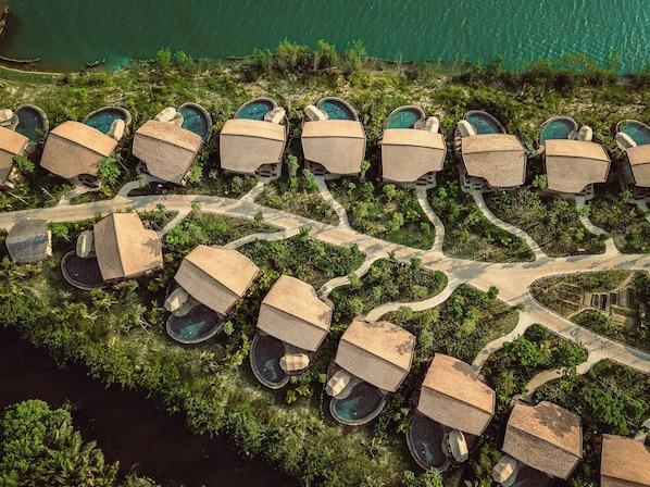 Une vue aérienne d’un complexe hôtelier comprenant plusieurs hébergements de type bungalow, chacun doté d’une piscine privée, le tout entouré d’une végétation luxuriante et traversé d’un sentier sinueux.