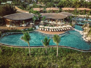 Ein Resort mit mehreren Pools, Liegebereichen und strohgedeckten Gebäuden.