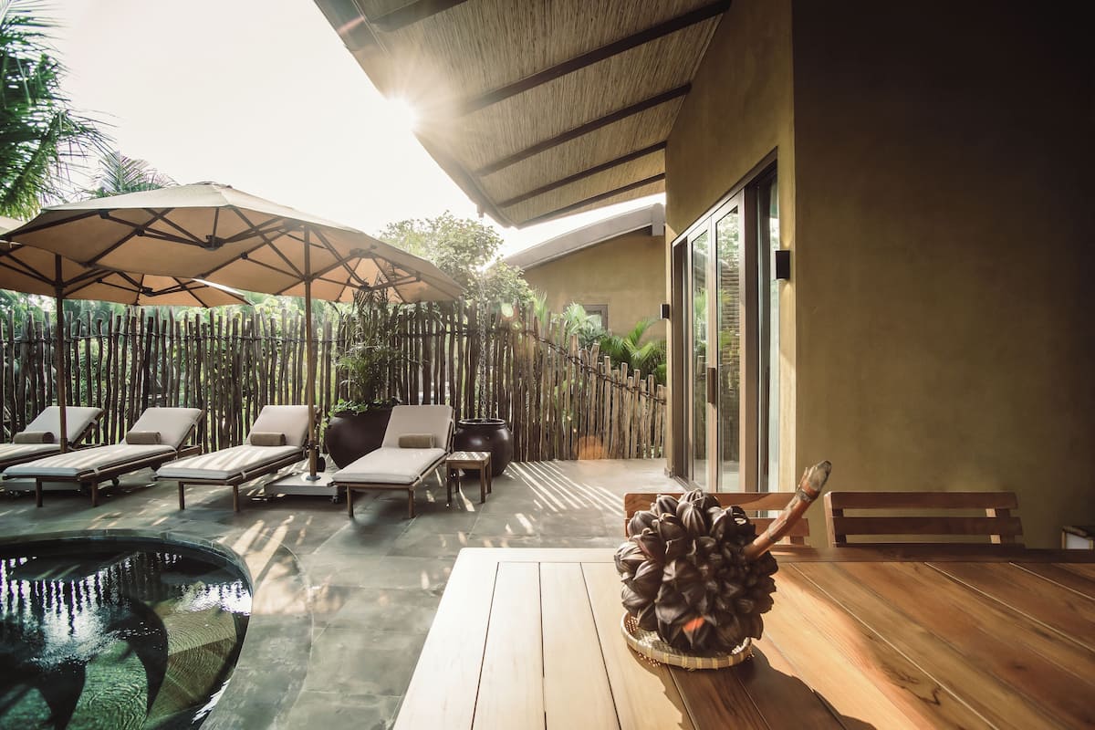 Un espacio al aire libre iluminado por el sol con sillones de relax, una mesa de madera y un centro de mesa decorativo.