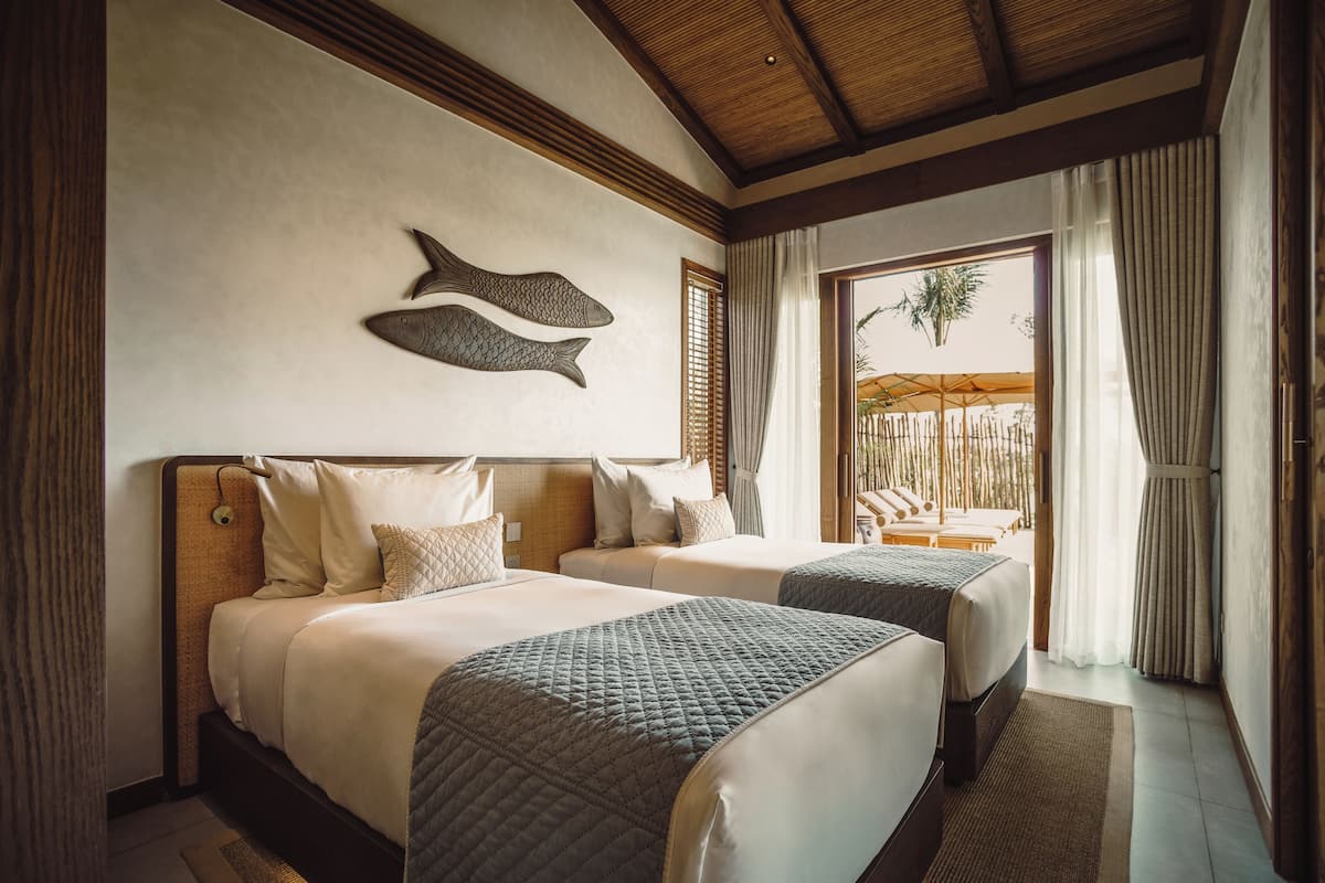 Habitación de hotel con dos camas, techo de madera, decoración de peces montada en la pared y vistas al exterior.