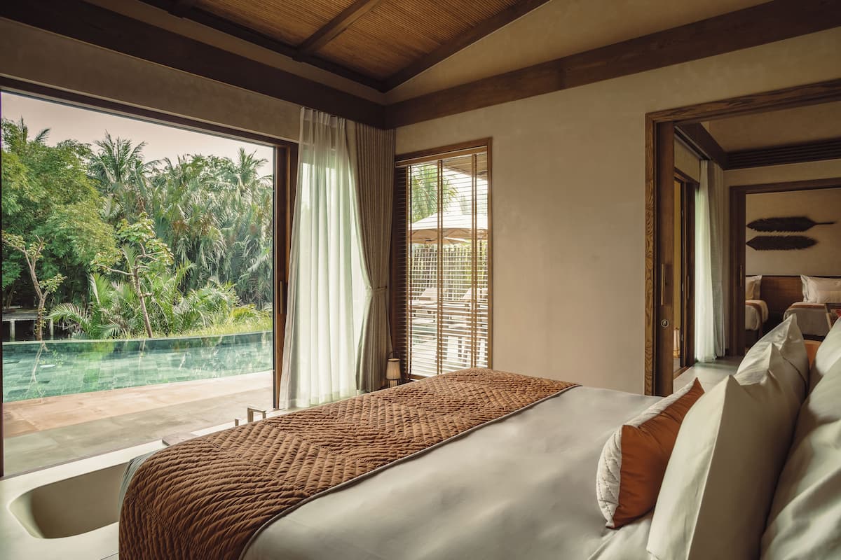 Un dormitorio con una cama grande, vista a una piscina y un jardín tropical afuera.