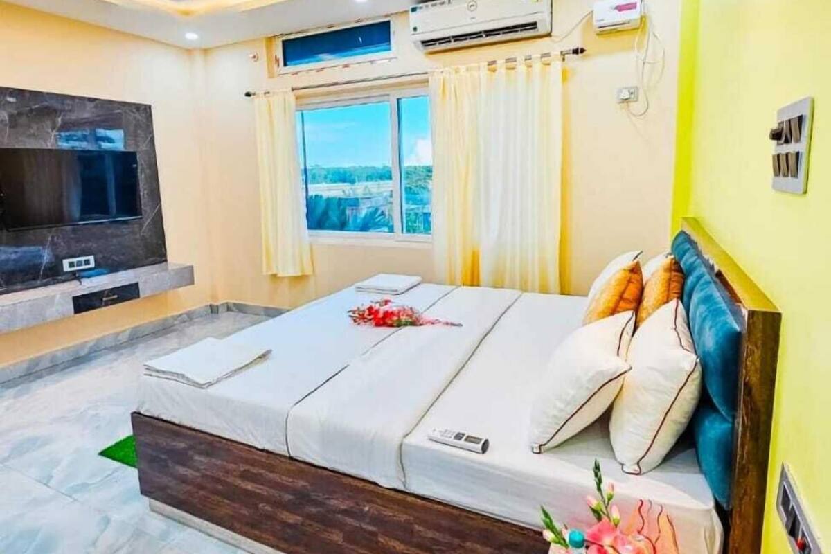 Quarto moderno com cama, TV, ar-condicionado e janela com cortinas.