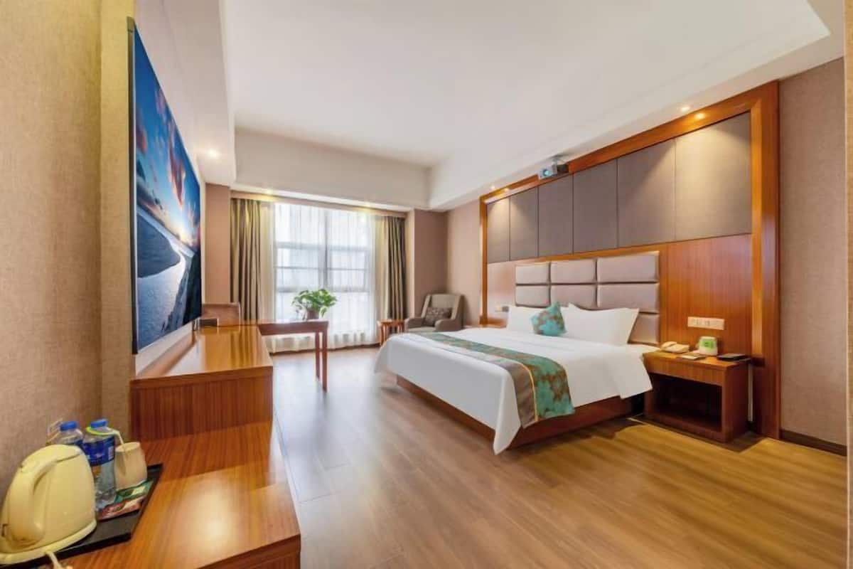 Habitación de hotel con cama, mesita de noche, silla, escritorio y un ventanal grande.