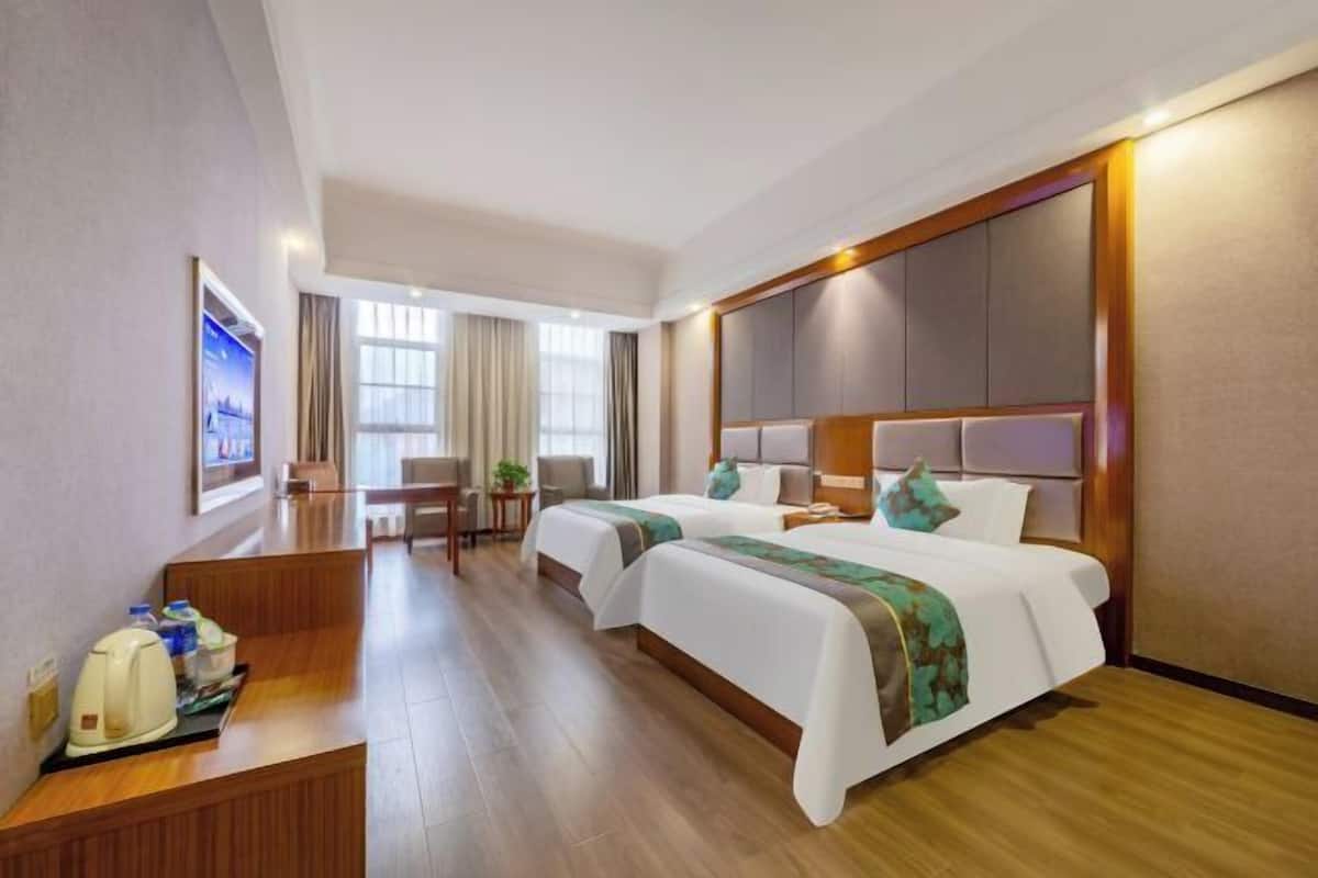 Habitación de hotel con dos camas, un escritorio, una silla y un ventanal grande.