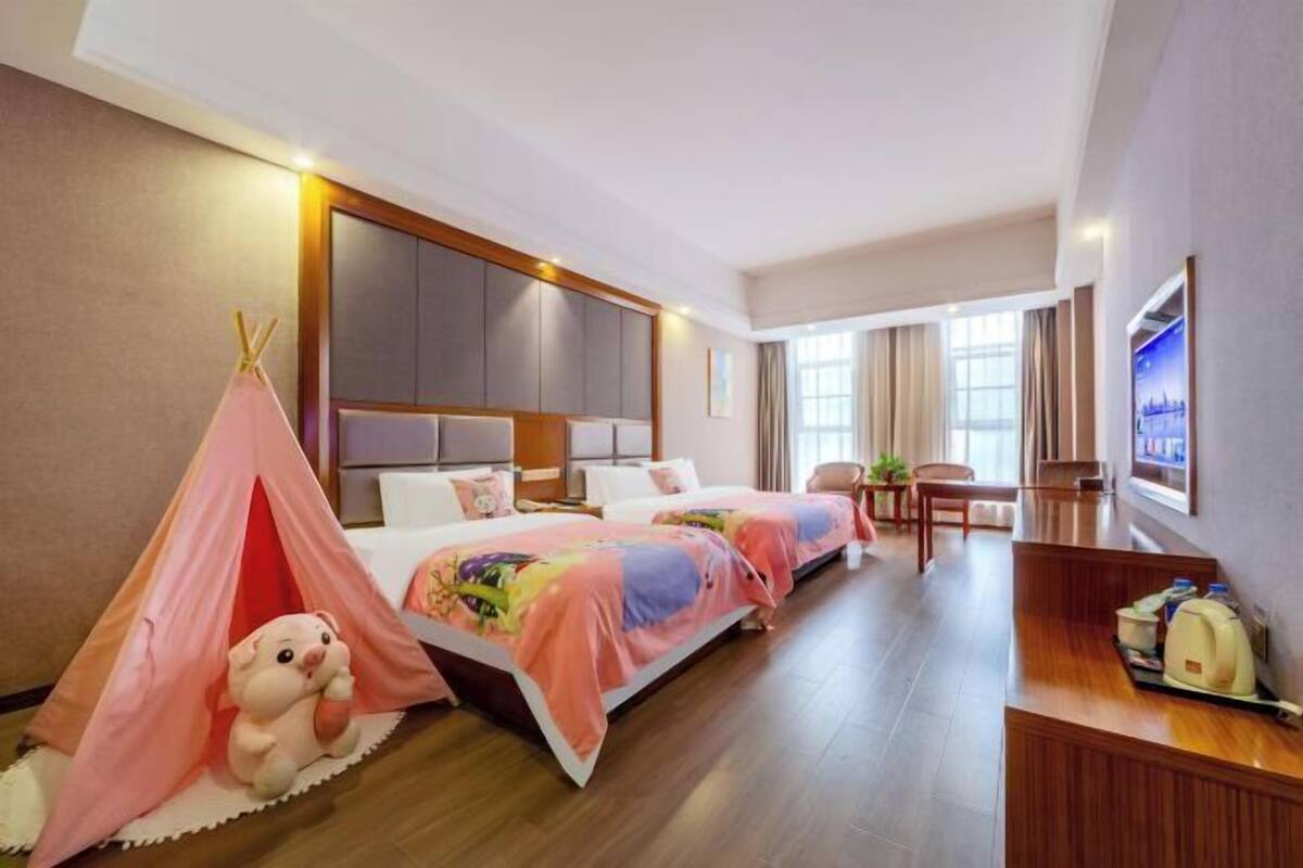 Habitación de hotel con dos camas, un escritorio, una silla, un televisor y un peluche en una tienda de campaña.