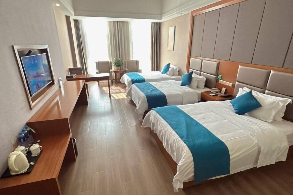 Habitación de hotel con dos camas, un escritorio, una silla, un televisor y una ventana con cortinas.