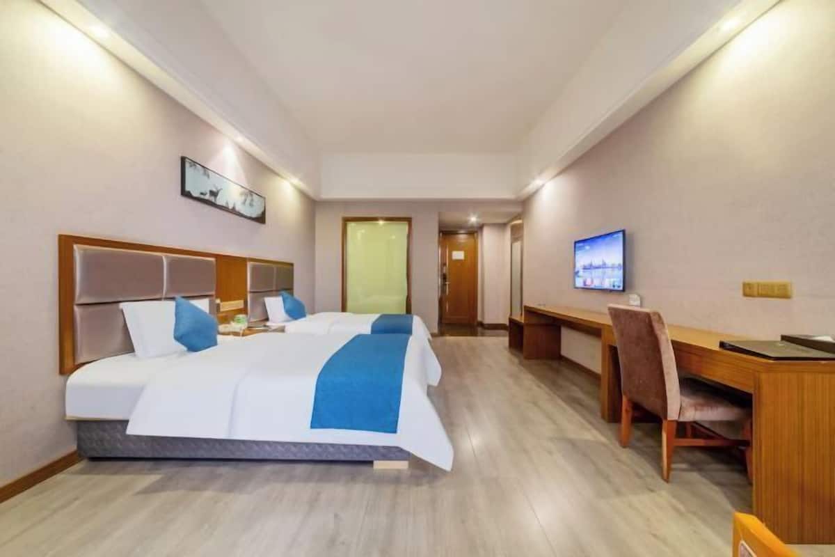 Una habitación de hotel con una cama grande, un escritorio, una silla, un televisor y una puerta que da a otra habitación.