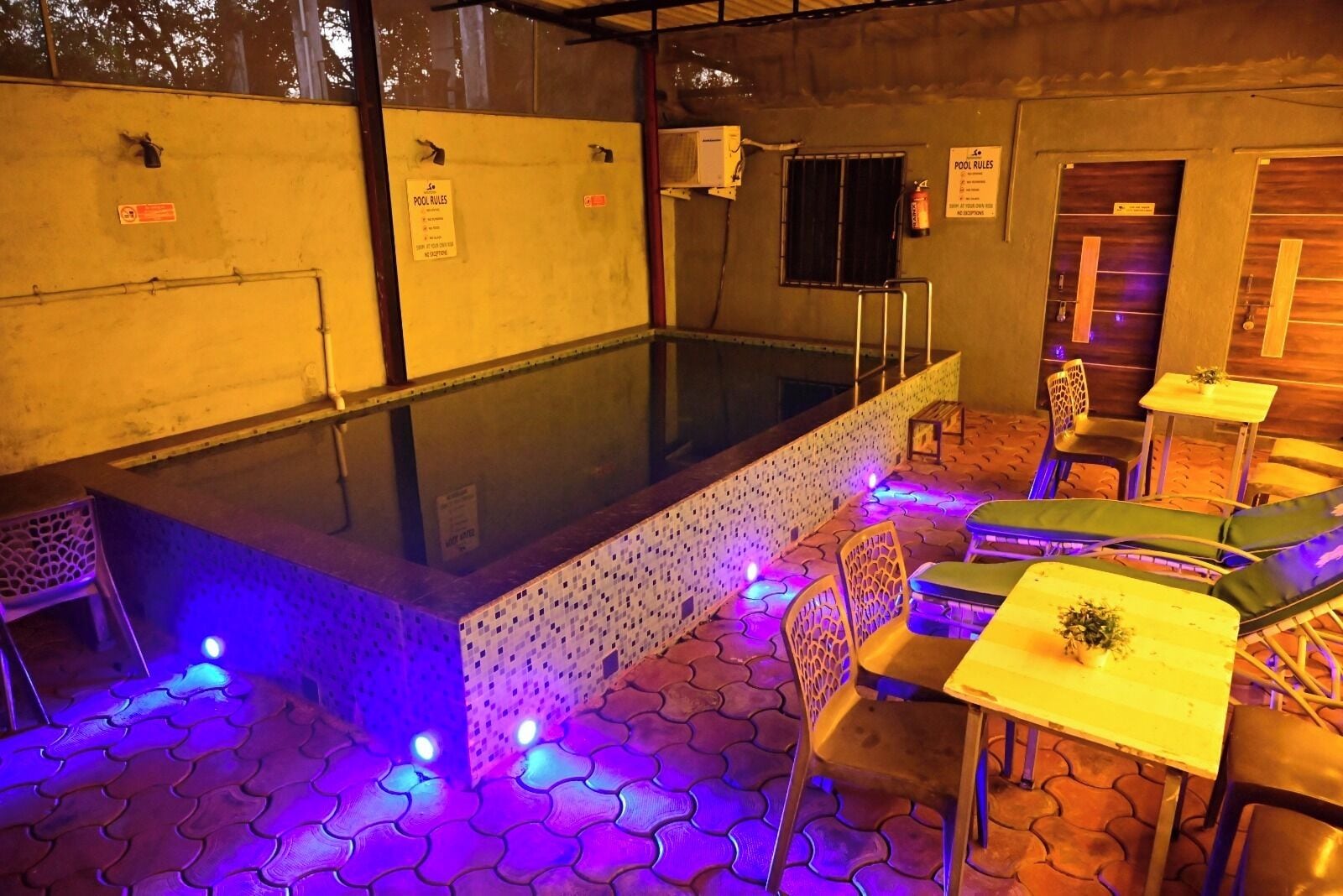 A pool area with seating and lounge chairs, a glass-enclosed pool, and a sign indicating pool rules.