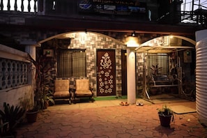 Un patio con piso de baldosas, dos sillas, una puerta con panel decorativo y una barandilla de metal.