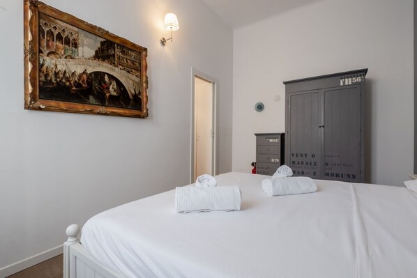 A hotel room with a bed, a painting, a wardrobe, and a door.