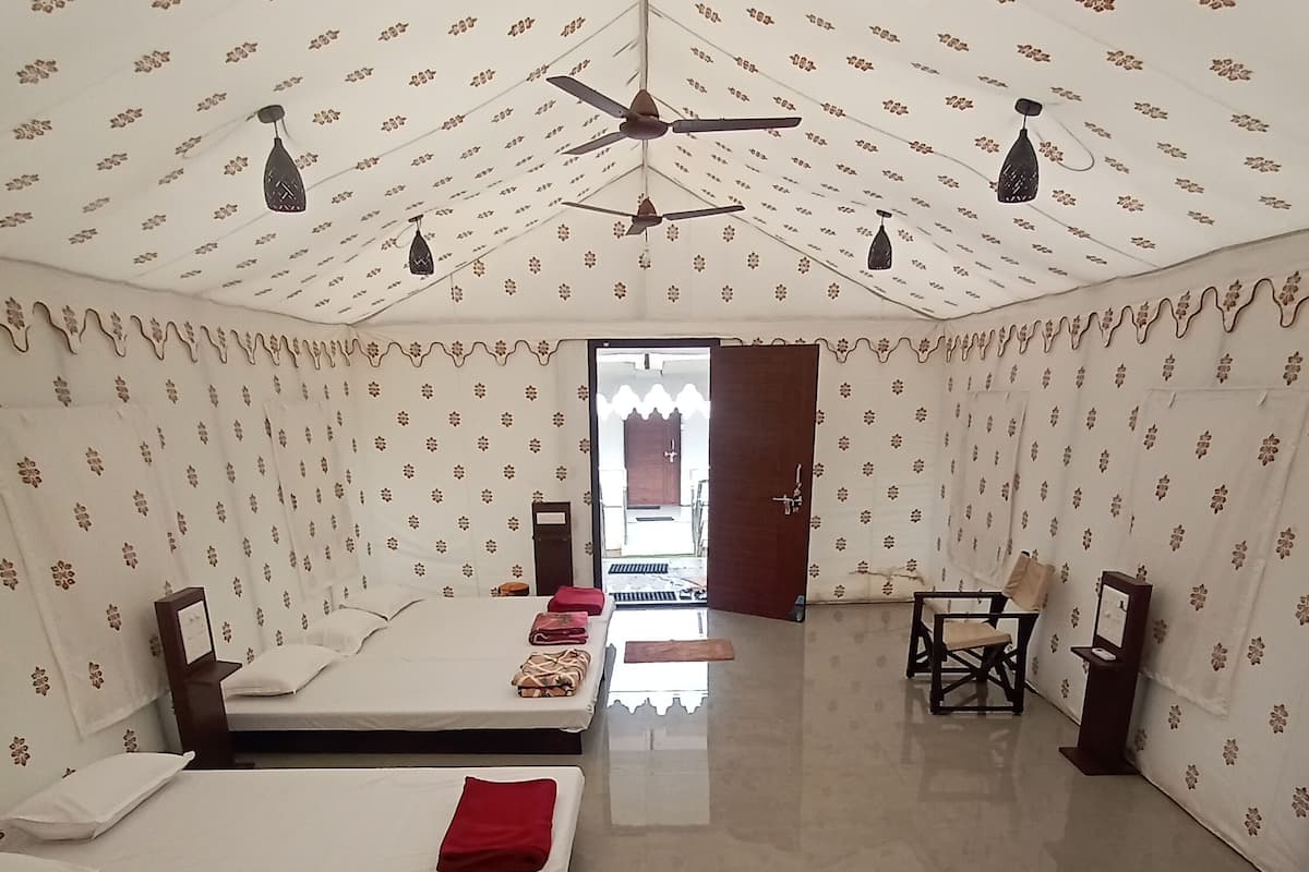 A room with a high ceiling, patterned wallpaper, a ceiling fan, and a bed with a red pillow.