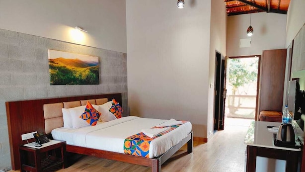 A bedroom with a wooden bed, a nightstand, a desk with a chair, and a view of the outdoors.