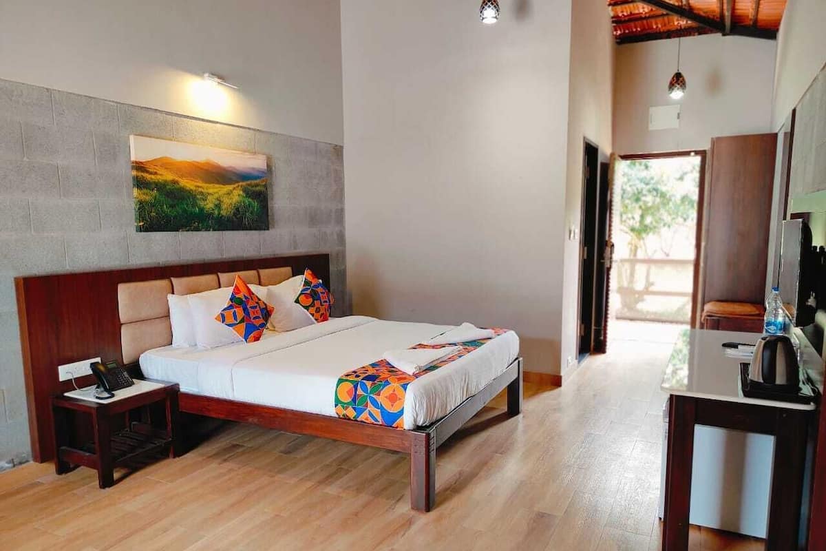 A bedroom with a wooden bed, a nightstand, a desk with a chair, and a view of the outdoors.