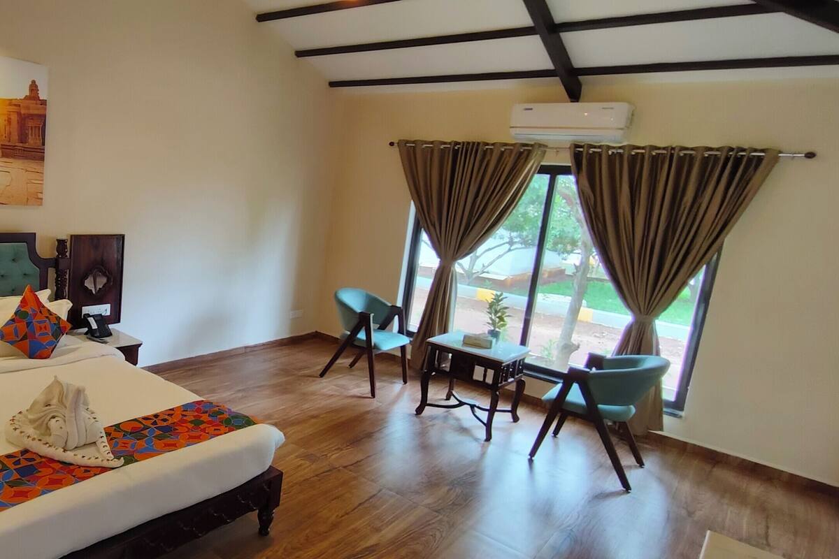 A hotel room with a large bed, a desk, two chairs, and a window with curtains.