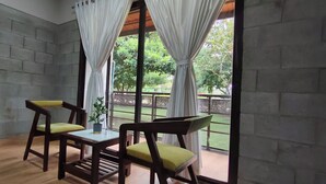 A hotel room with a bed, two chairs, a small table, and a view of a garden through large windows.