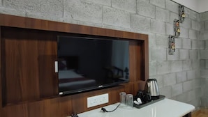 A television mounted on a wooden panel with a coffee maker and glasses on a tray below.