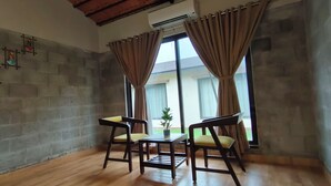 A room with a stone wall, two wooden chairs, a small table, and a window with curtains.