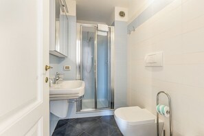 Un baño con ducha, lavamanos, inodoro y perchero para toallas.