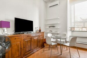 Una sala de estar moderna con un televisor de pantalla plana, armarios de madera, una mesa de vidrio, sillas blancas y un ventanal con vistas.