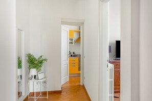 Een gang die uitkomt op een keuken met witte muren, een betegelde vloer en een kleine tafel met planten.